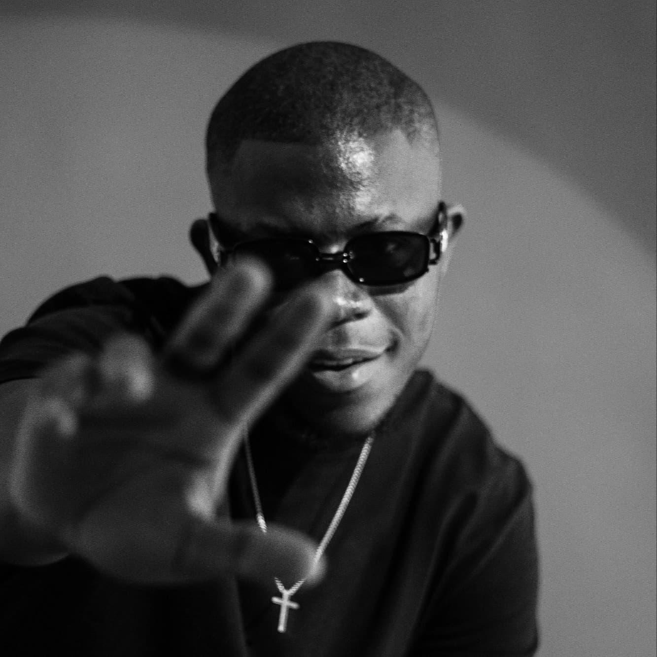 Black and white portrait of TAPIWA in sunglasses, one hand held out toward the camera